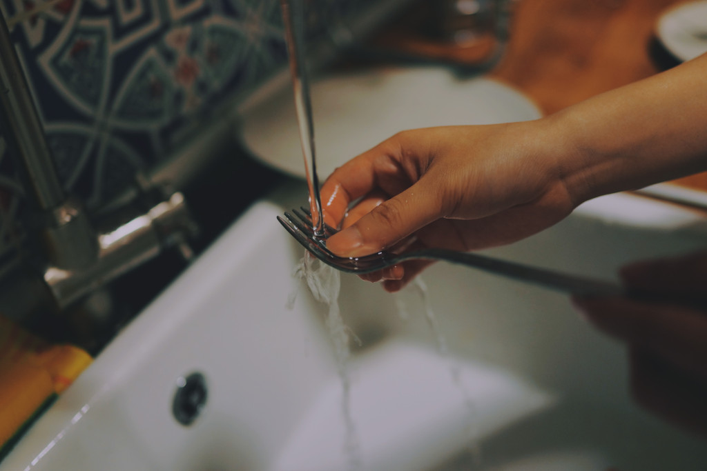 mano lavando con agua un tenedor